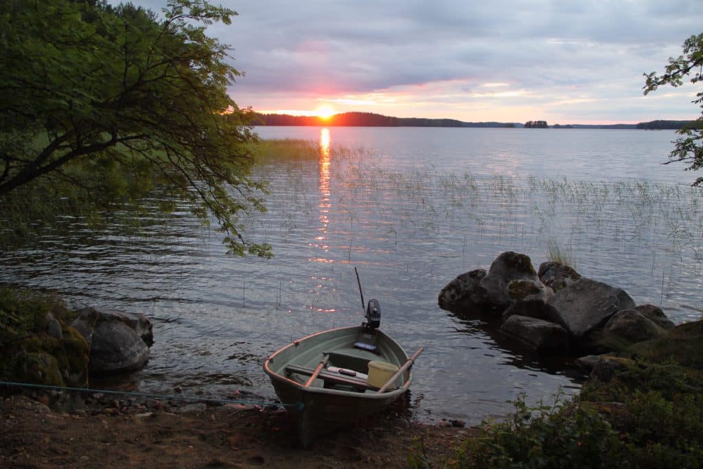 Auringonlasku taustalla, etulalla vene. Aholan mökit Padasjoki.