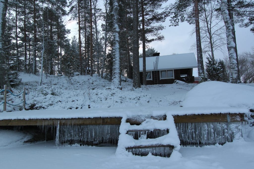 Jäätynyt laituri etualalla, mökki taustalla. Aholan mökit Padasjoki.